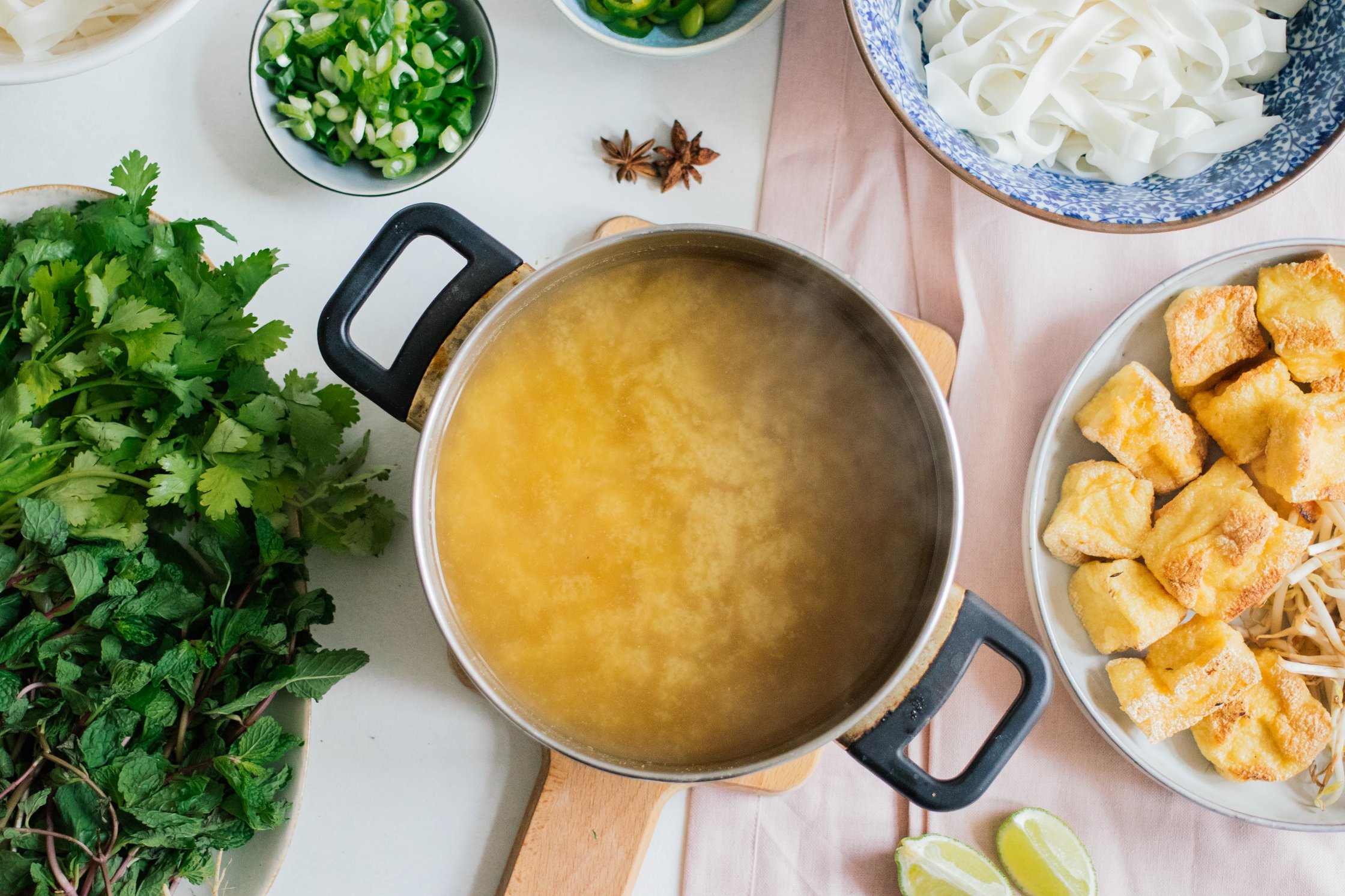 vegetable stock and toppings for vegan pho on a table
