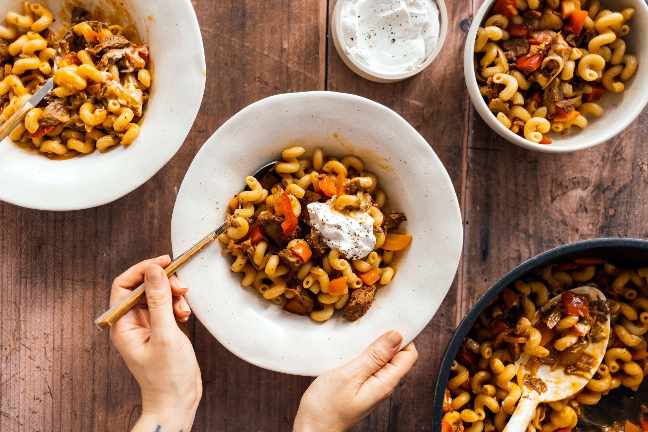 holding a plate of Vegan Seitan Goulash with Bell Peppers and Pasta
