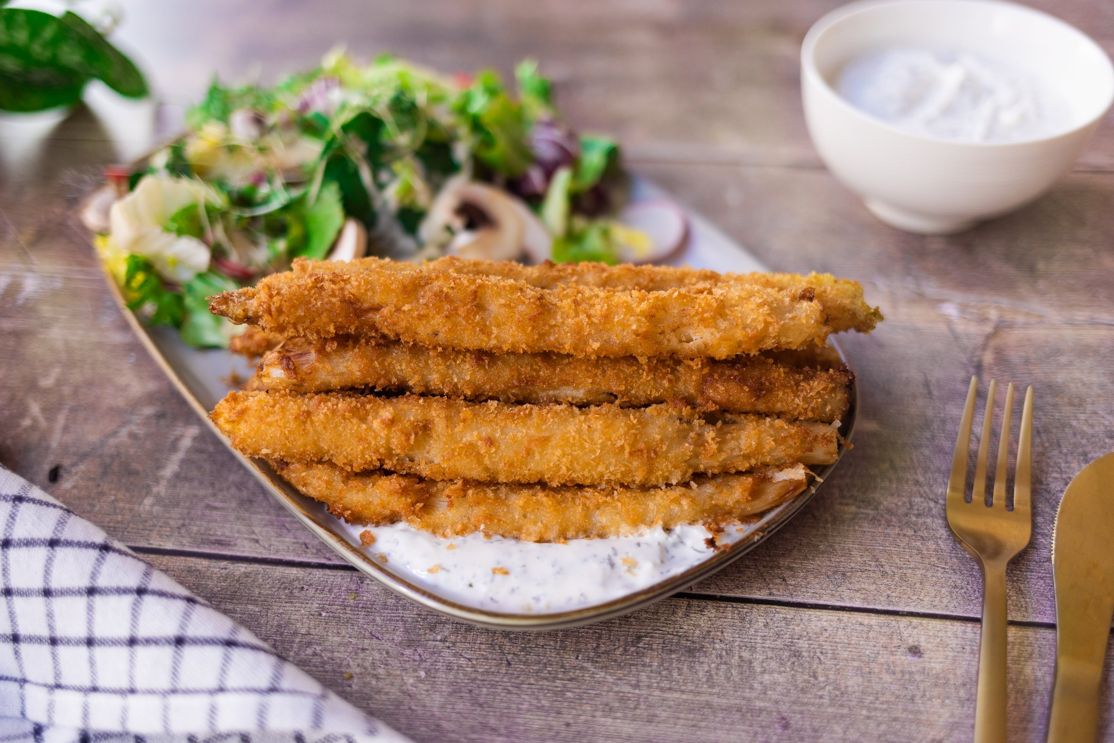 Fried asparagus with vegan yogurt dip and spring salad arranged on a plate.