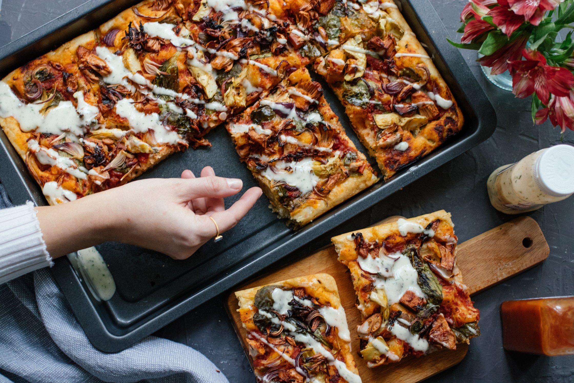 a hand grabs a piece of vegan bbq sheetpan pizza