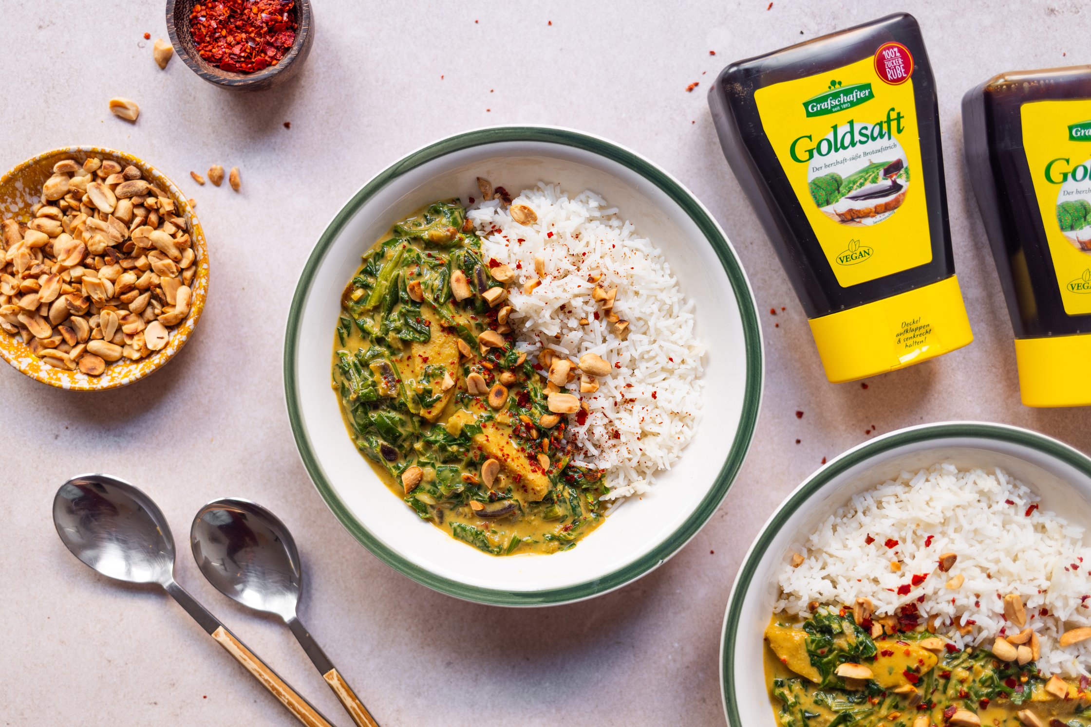 fertiges erdnuss-hühnchen-curry auf einem Teller, drumherum stehen geröstete Erdnüsse, chiliflocken in Schüsseln 
goldsaft vo