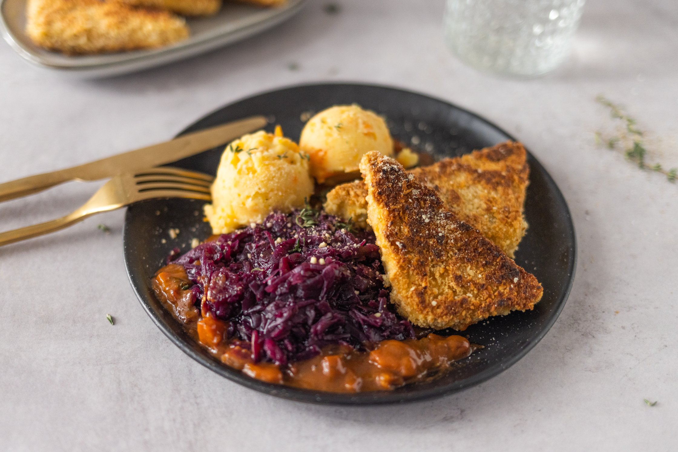 Tofu with vegan parmesan crust, mashed potatoes and carrots & red cabbage on a plate, cutlery, glass and kitchen towel