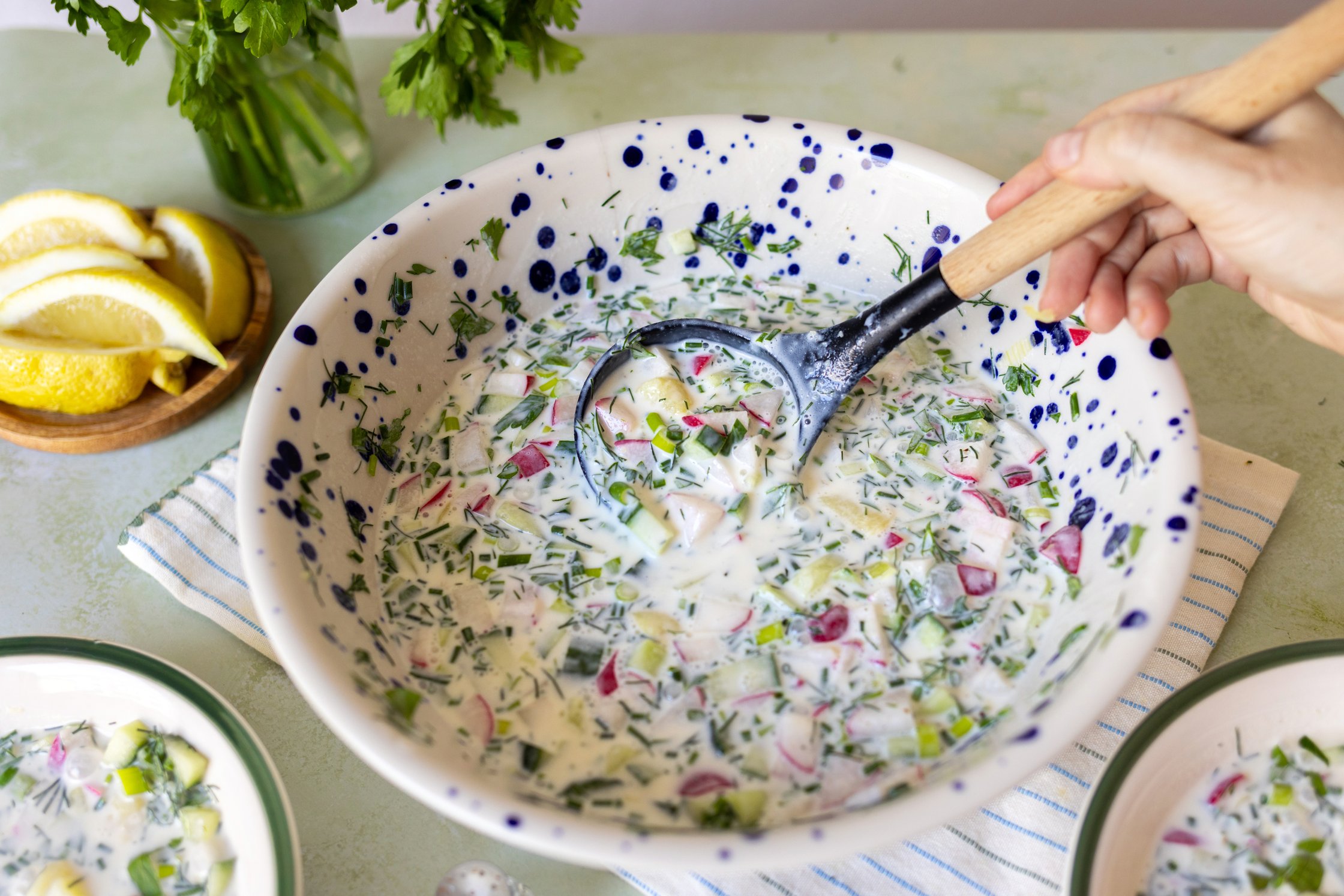Top-Shot von der Okroschka. Eine Hand rühren mit einer Kelle in der Suppe.