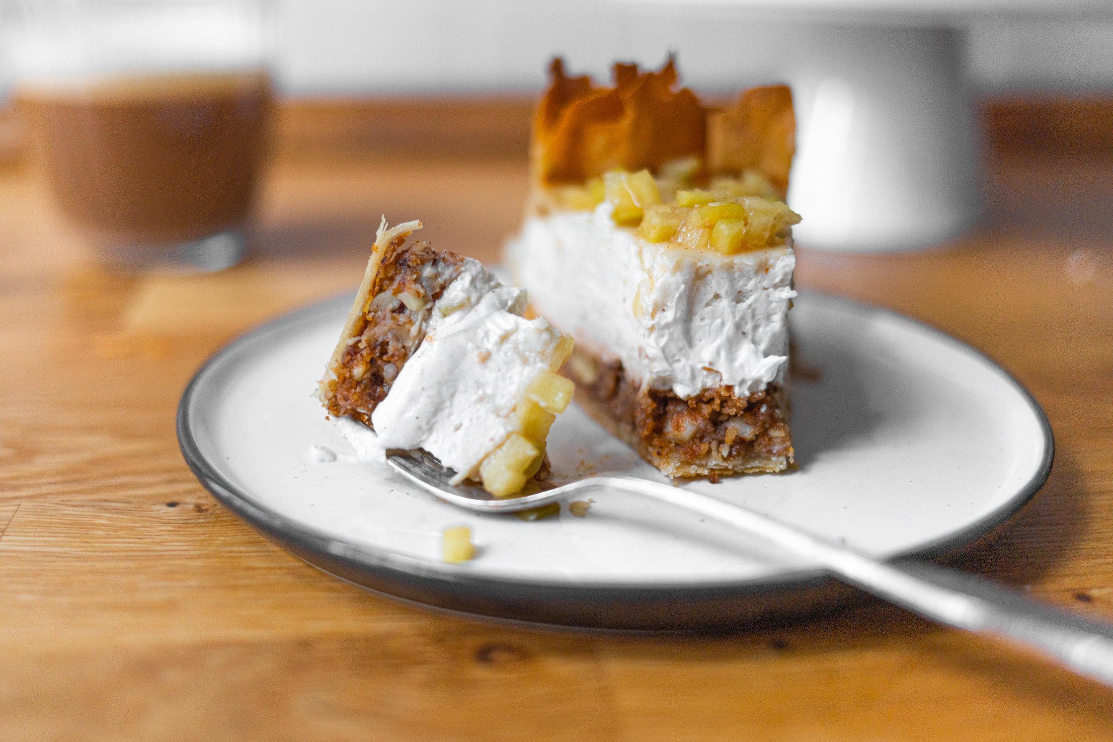 veganer Käsekuchen auf einem Teller, Kuchengabel, kaffee im Hintergrund