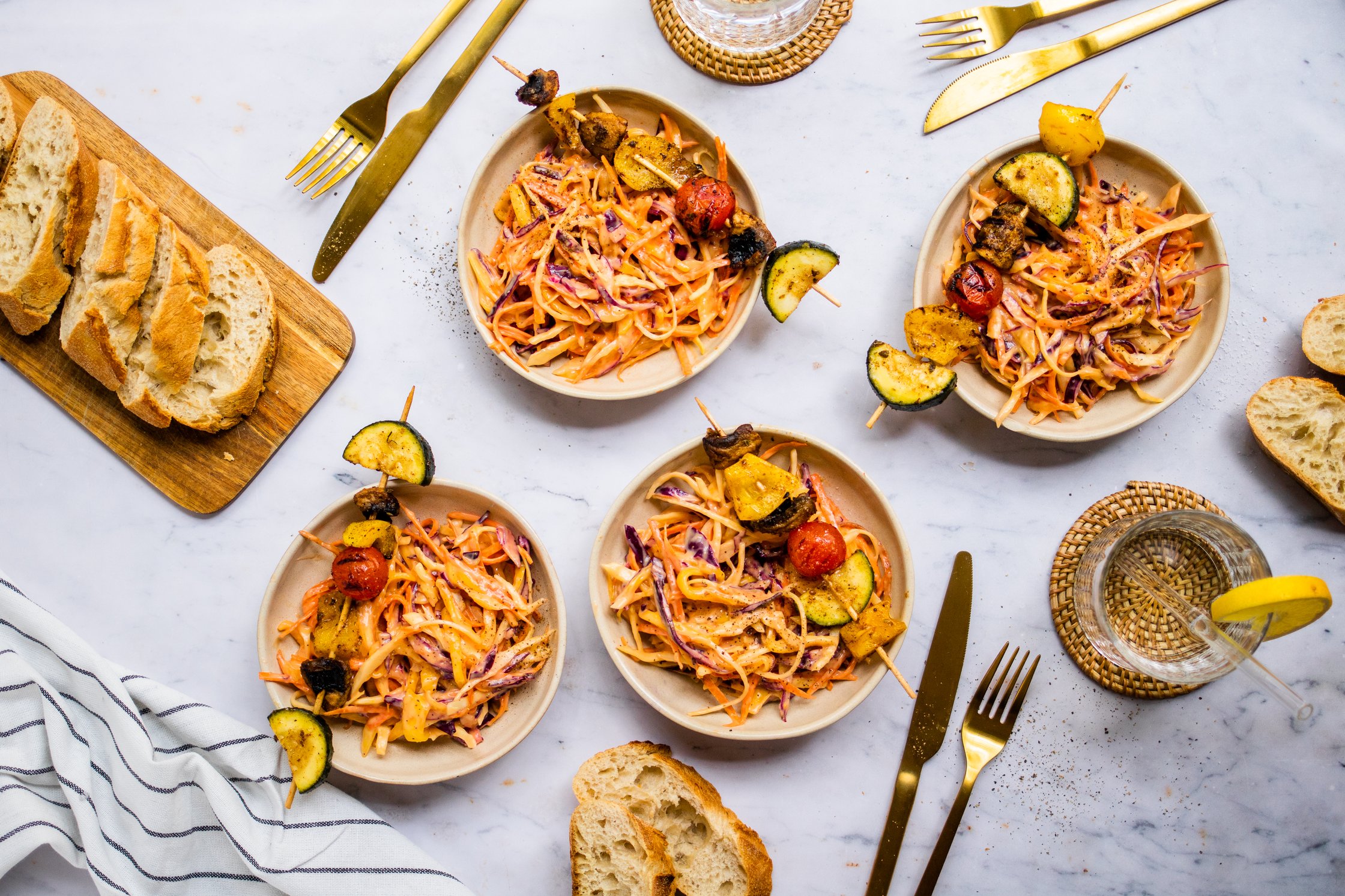 Vegan Mango Coleslaw on Plates with Vegetable Skewers, Baguette, Glas of Water with Lemon