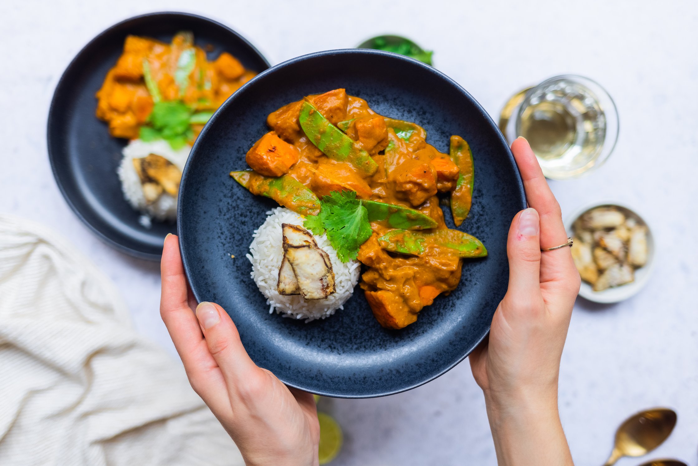 A plate of vegan pumpkin curry with rice and ginger chips is held in front of the camera