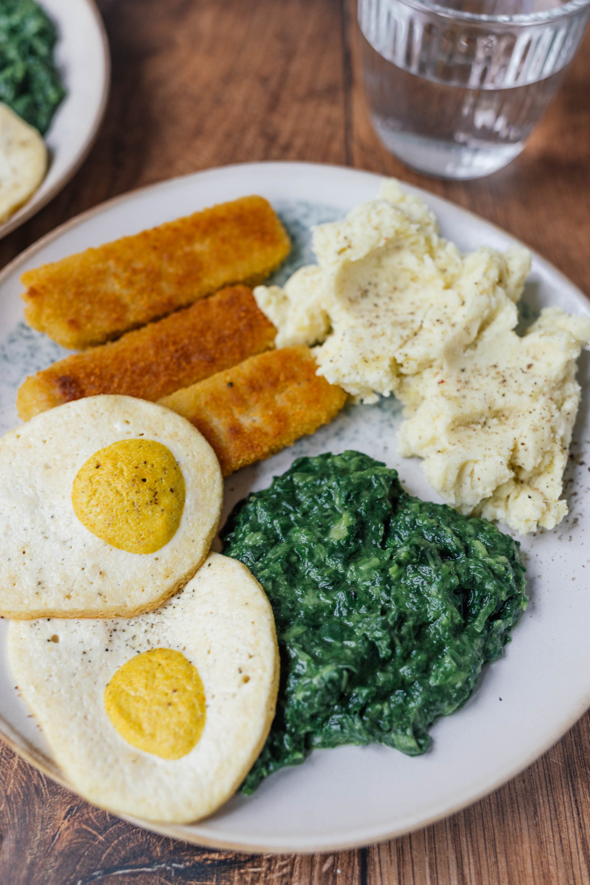 mashed potatoes with creamed spinach, vegan fried eggs and vegan fish fingers on a plate