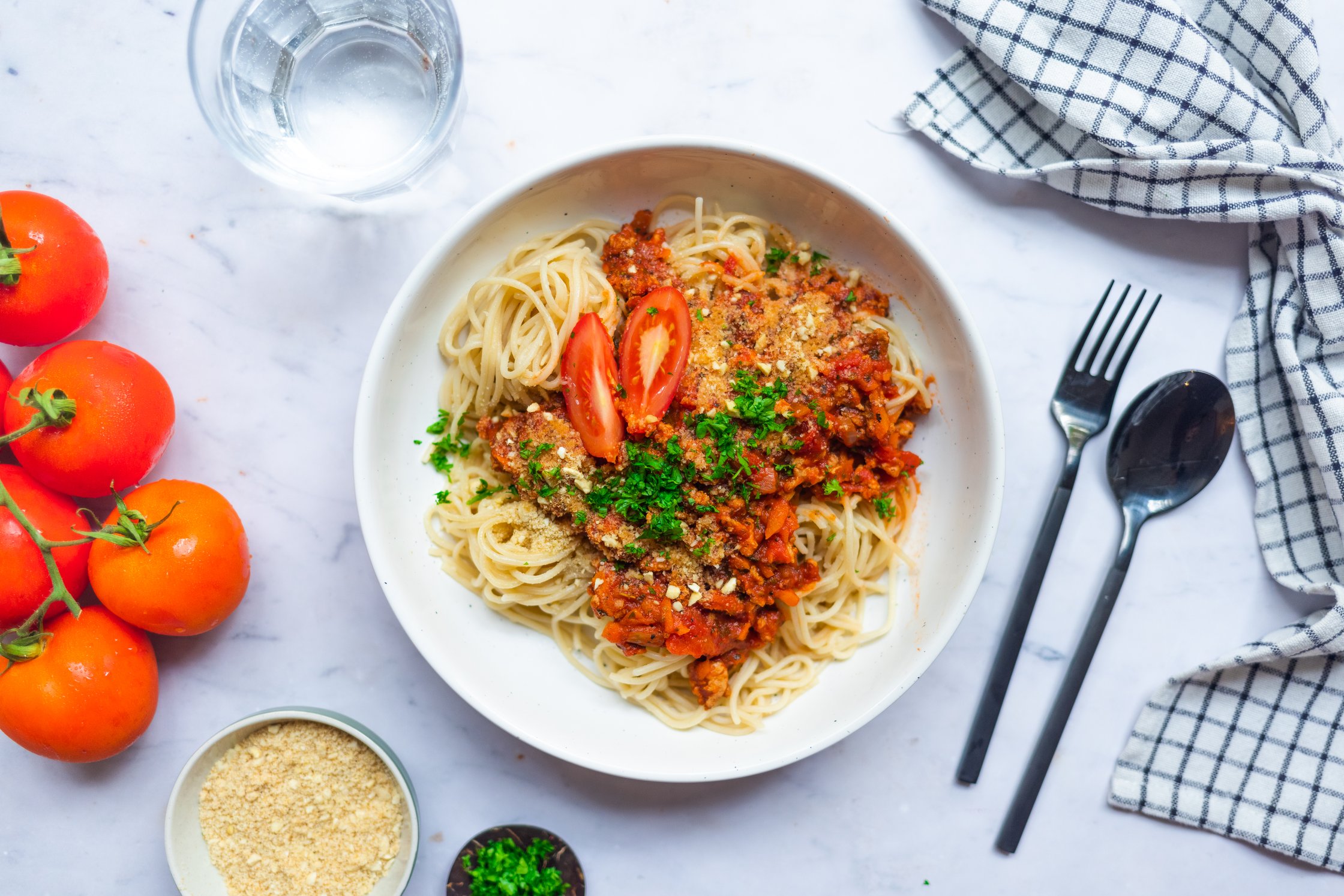 Vegan spaghetti bolognese topped with tomatoes, fresh parsley and homemade parmesan cheese