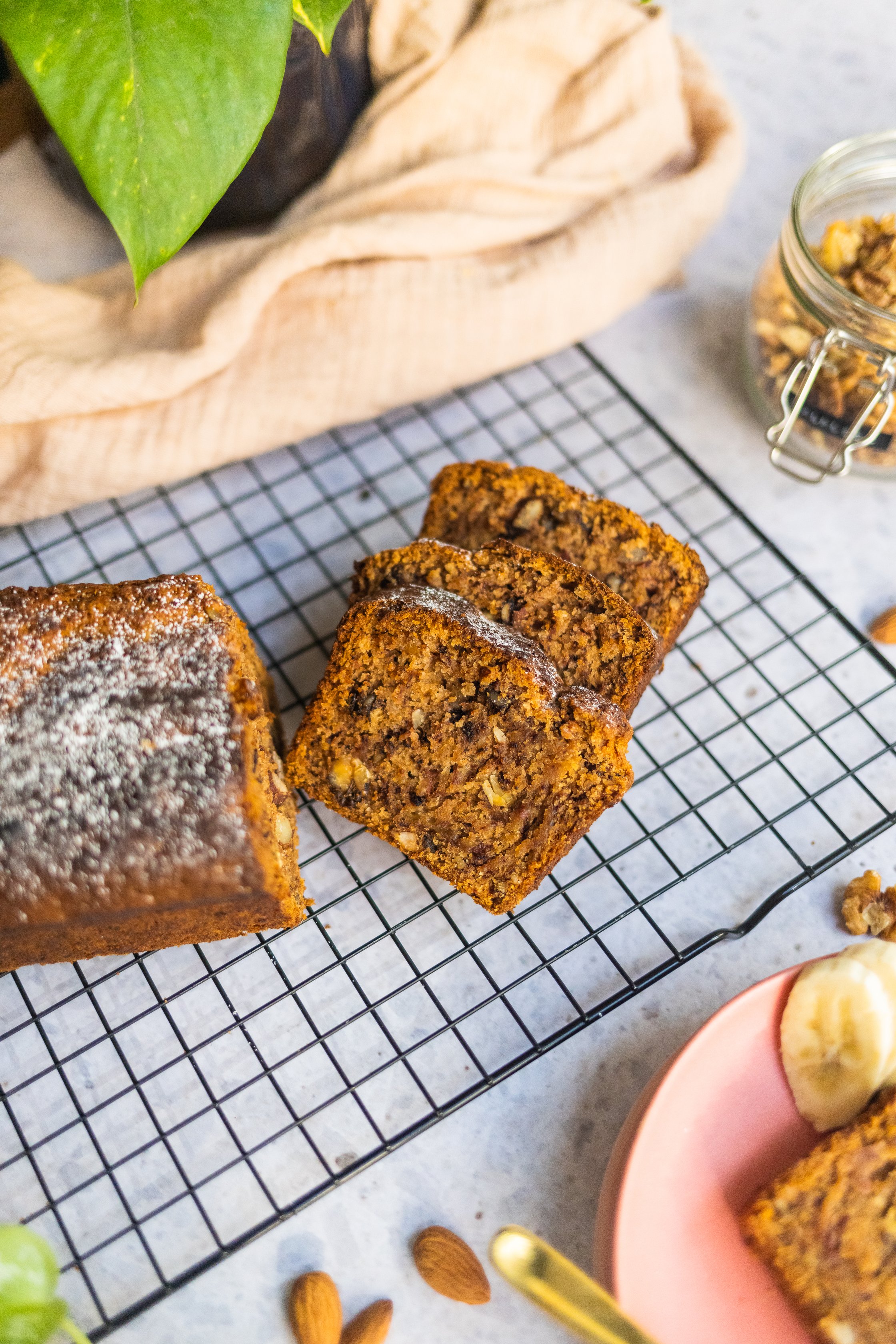vegan banana bread on a rack, next to it is a kitchen towel and some almonds