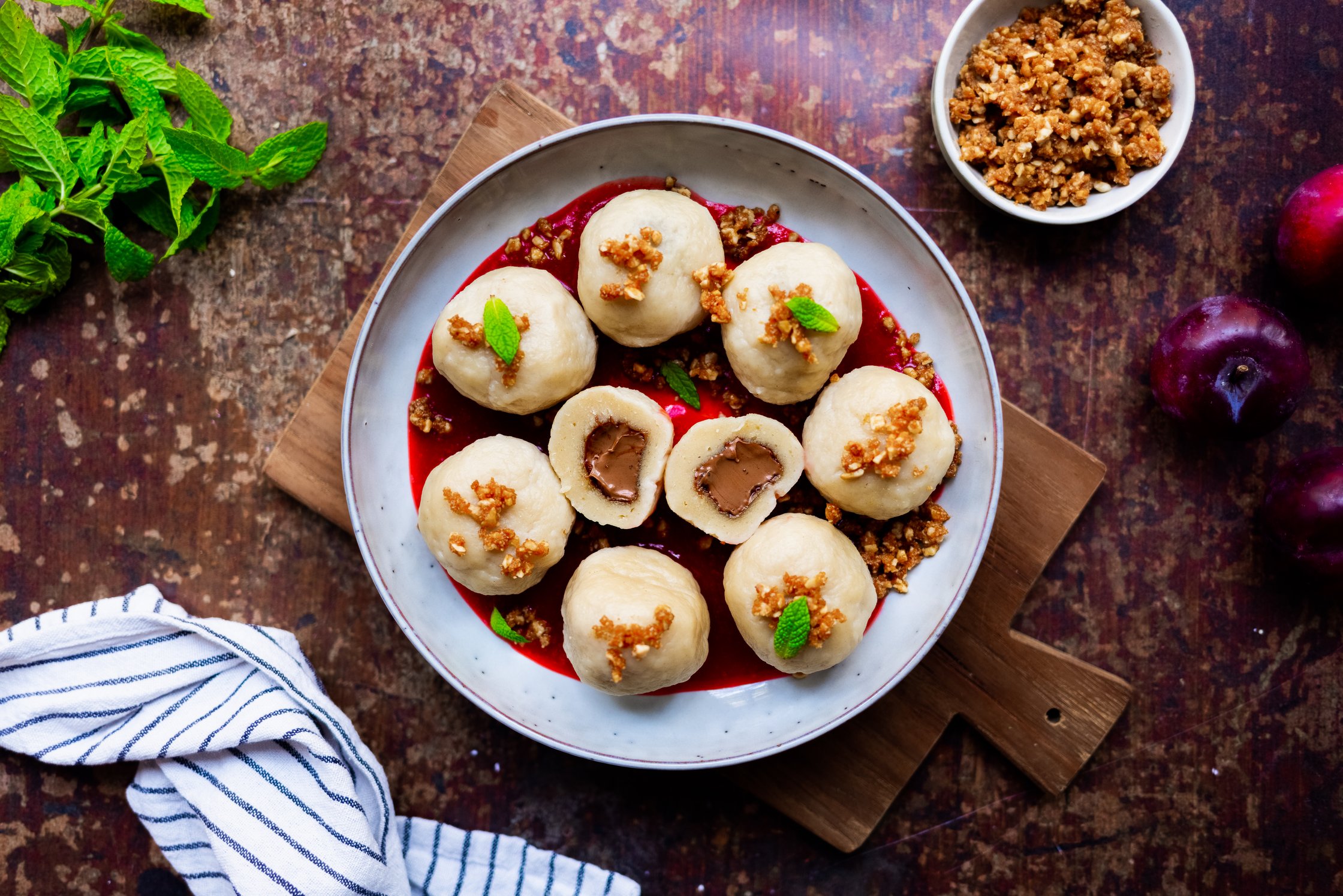 Vegane Nougatknödel mit Zwetschgensoße in einer Schale angerichtet vor einem dunklen Hintergrund.