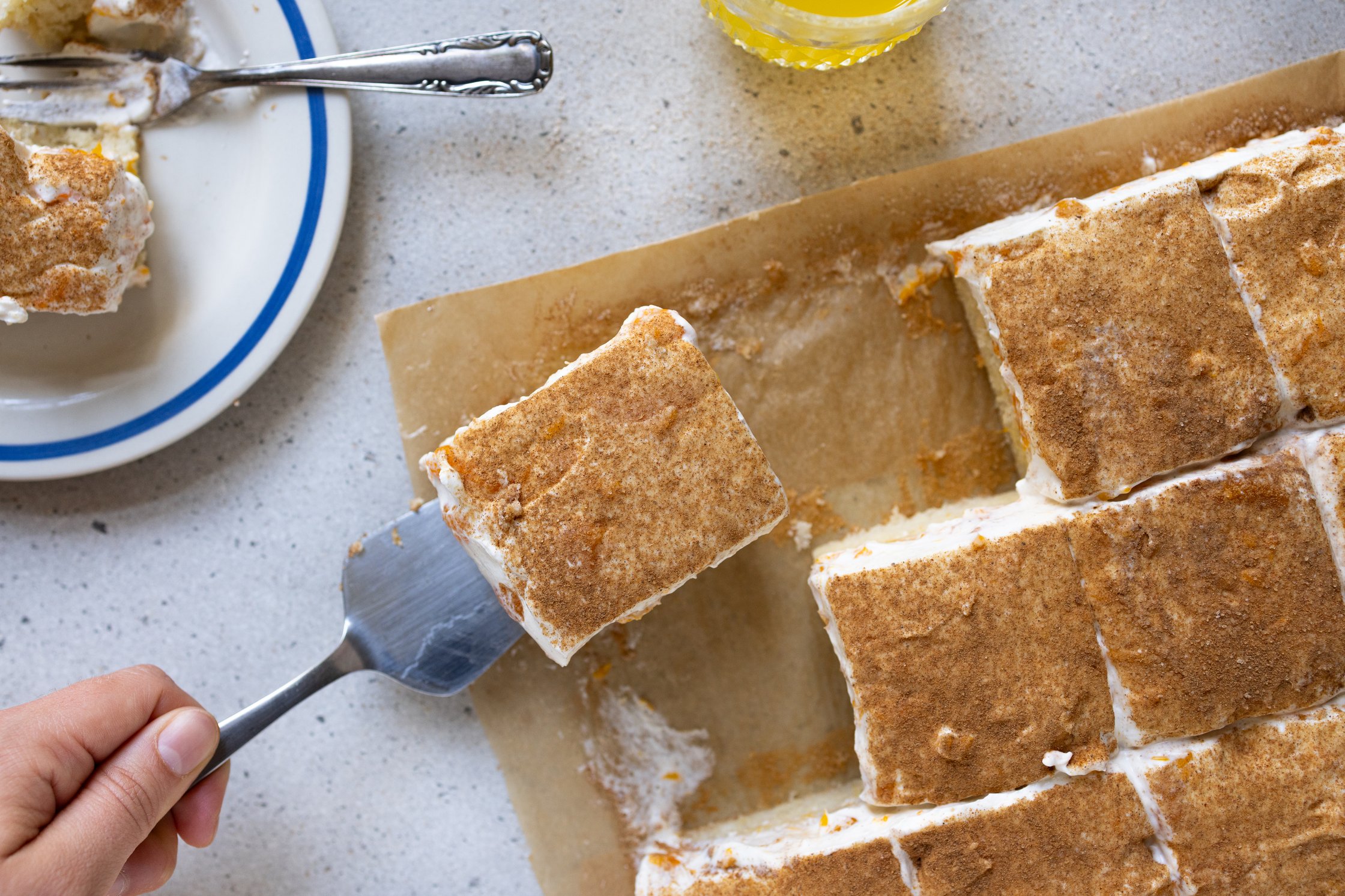 Der fertige Fantakuchen von oben mit dicker Zimt-Zucker-Schicht. Eine Ahn hebt mit einem Kuchenheber ein Stück vom Backpapier