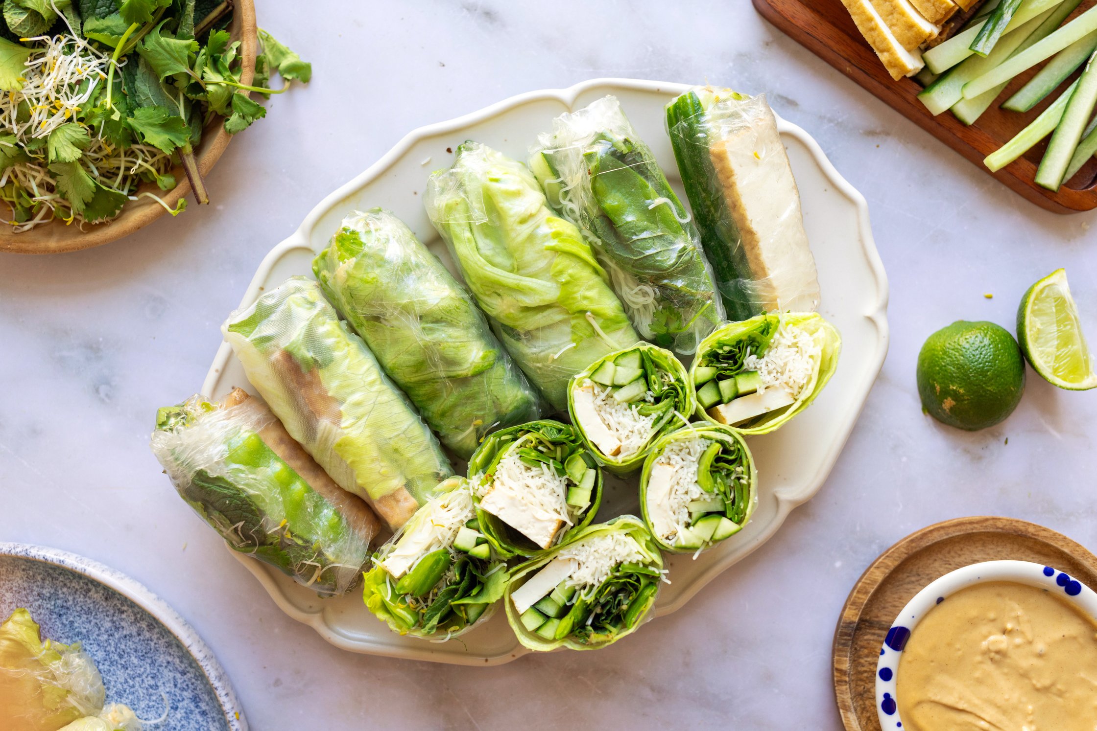 A platter of green summer rolls filled with sugar snap peas, cucumber, tofu, rice noodles, lettuce, bean sprouts and mint. Al