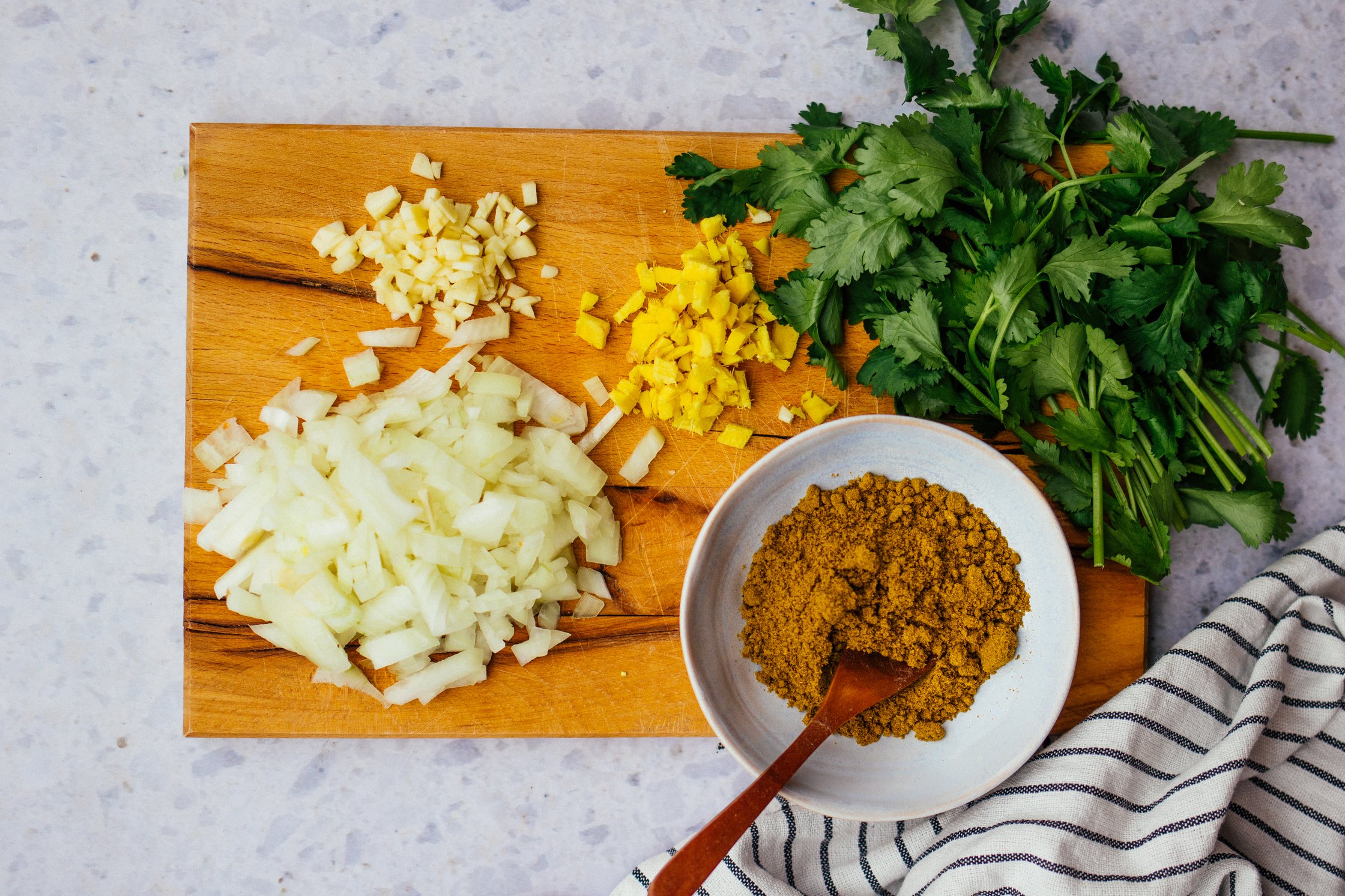 A wooden cutting board with prepped ingredients for vegan chicken madras – a bowl of madras curry powder, fresh cilantro, dic