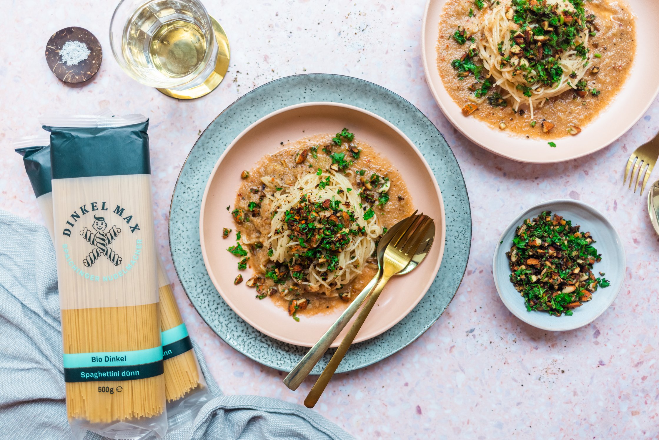 Zwei Teller Dinkel-Spaghetti in veganer brauner Buttersauce mit Petersilien-Mandel-Topping vor einem hellen Untergrund