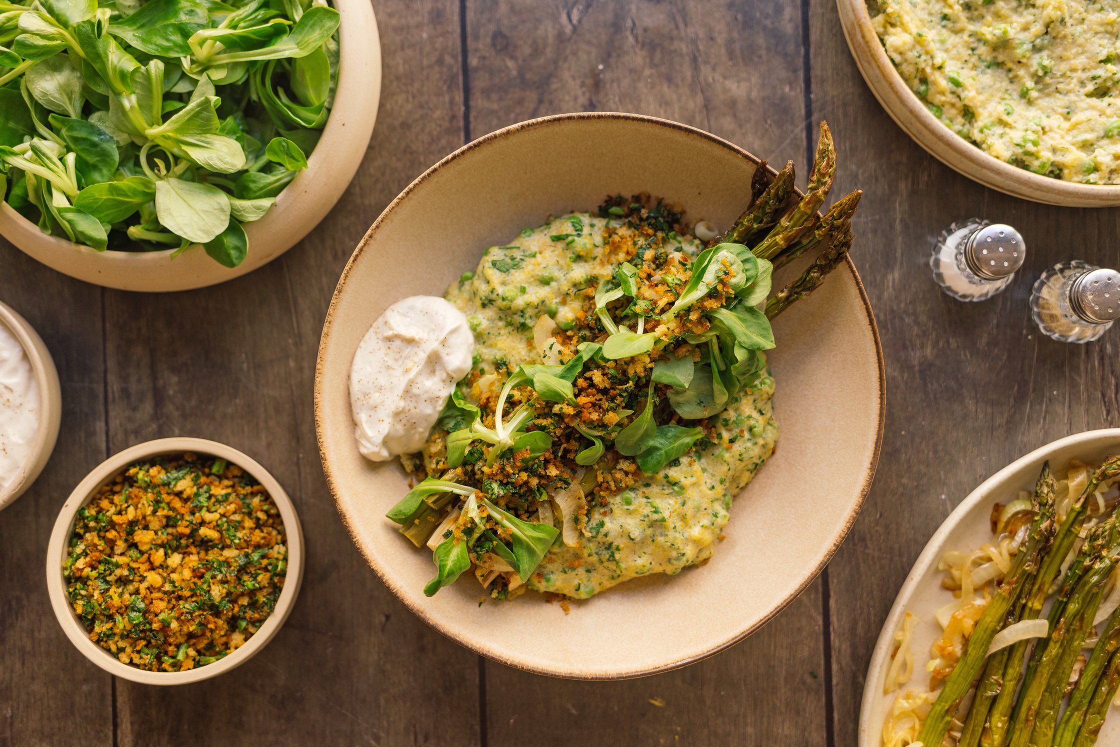 Cremige Zitronen-Polenta mit grünem Spargel, Kräutern und vegane Butterbrösel serviert auf dem tisch