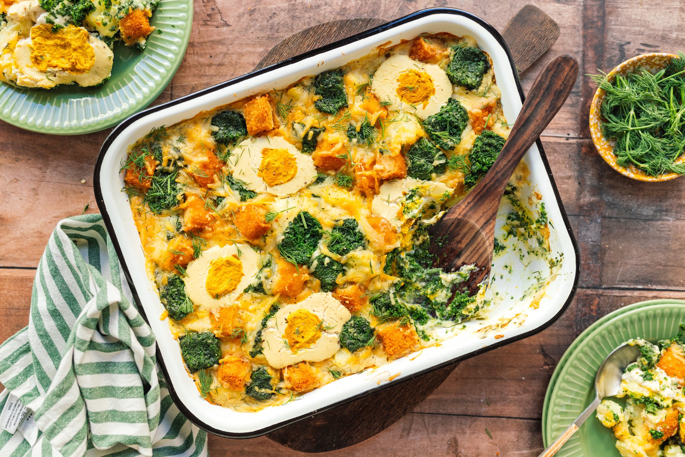 Veganer Kartoffel-Spinat-Fischstäbchen-Auflauf mit „Ei“ serviert auf dem tisch