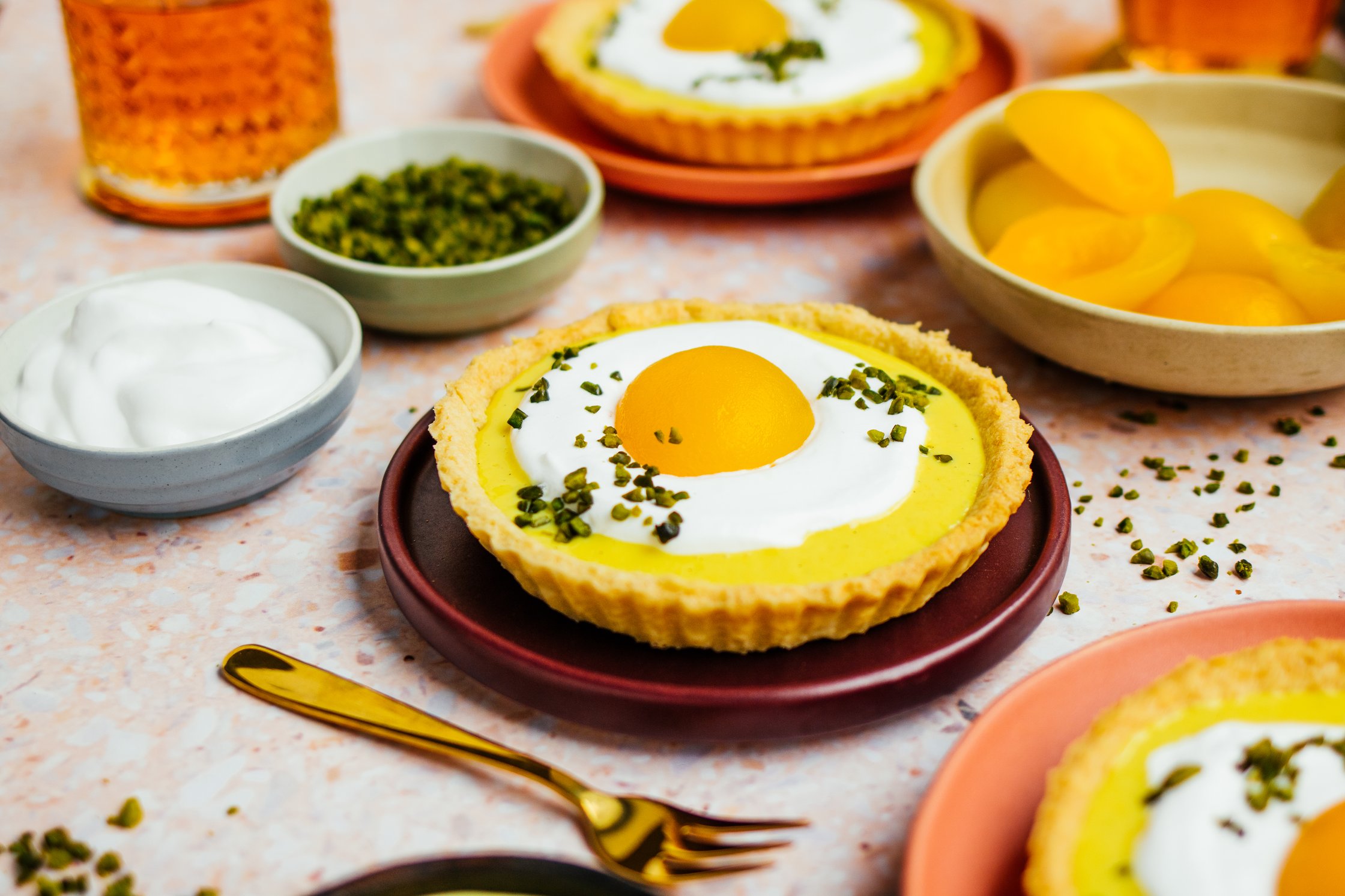 Veganes Oster-Eierlikör-Tartelette mit gehackten Pistazien, veganer Sahne und Aprikosen auf Tellerchen
